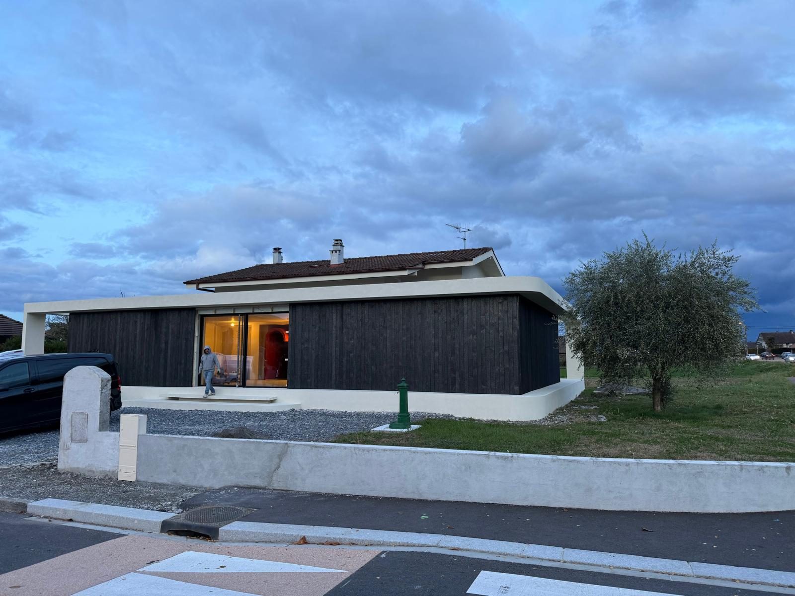 Façade habillée de bois teinté sombre au crépuscule, réalisation Trend Reno